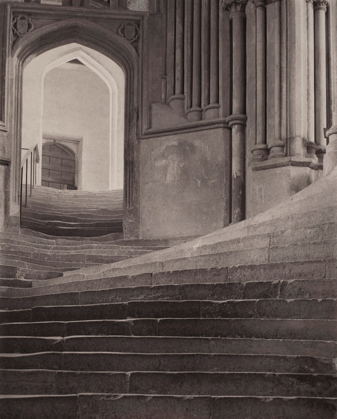 photograph. Two sets of stone stairs ascend in different directions. The low angle of the photographer makes the staircase on the right appear to curve, and highlights the warped form of the steps on the left, worn wavy by footsteps